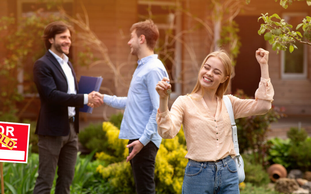 Happy young woman with house key and her husband shaking hands with Real Estate Agent in backyard